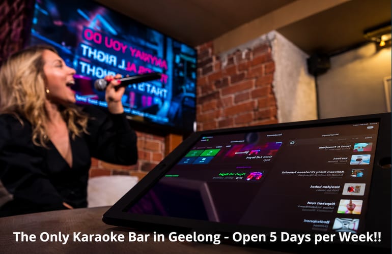 A singer with a microphone at Here & Now Lounge, with the karaoke song-selection tablet in the foreground